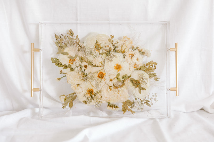 A white and green wedding bouquet pressed and preserved in a serving tray with gold handles. 