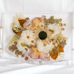 A fall-toned wedding bouquet preserved in a resin serving tray with gold handles. 