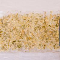 A resin serving tray with green leaves, white flowers, and gold metallic flakes designed like confetti. The tray has black handles and is against a white background. 