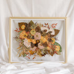 A fall-toned wedding bouquet that has been pressed into a gold wood frame as a bouquet preservation service.