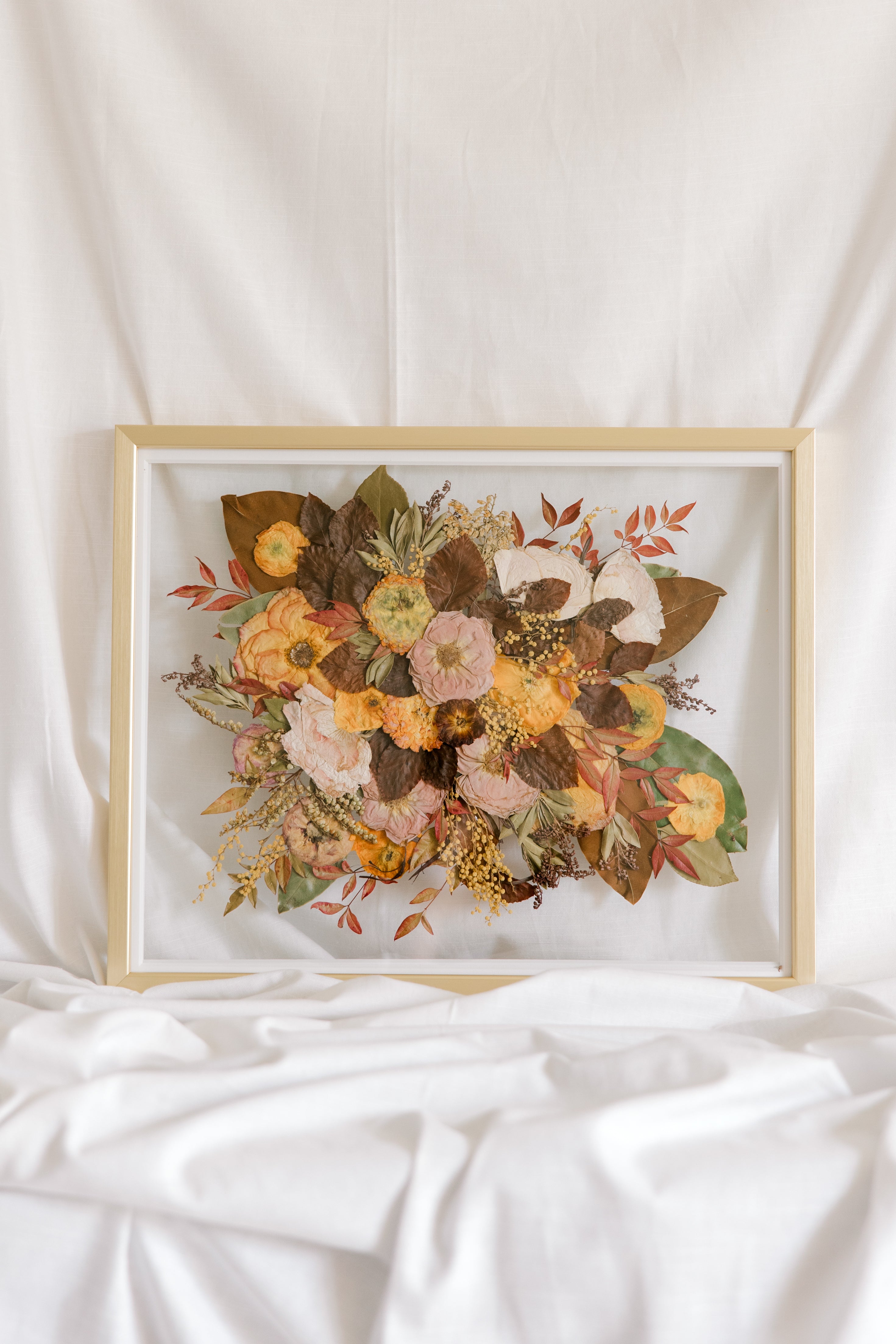 A fall-toned wedding bouquet that has been pressed into a gold wood frame as a bouquet preservation service.