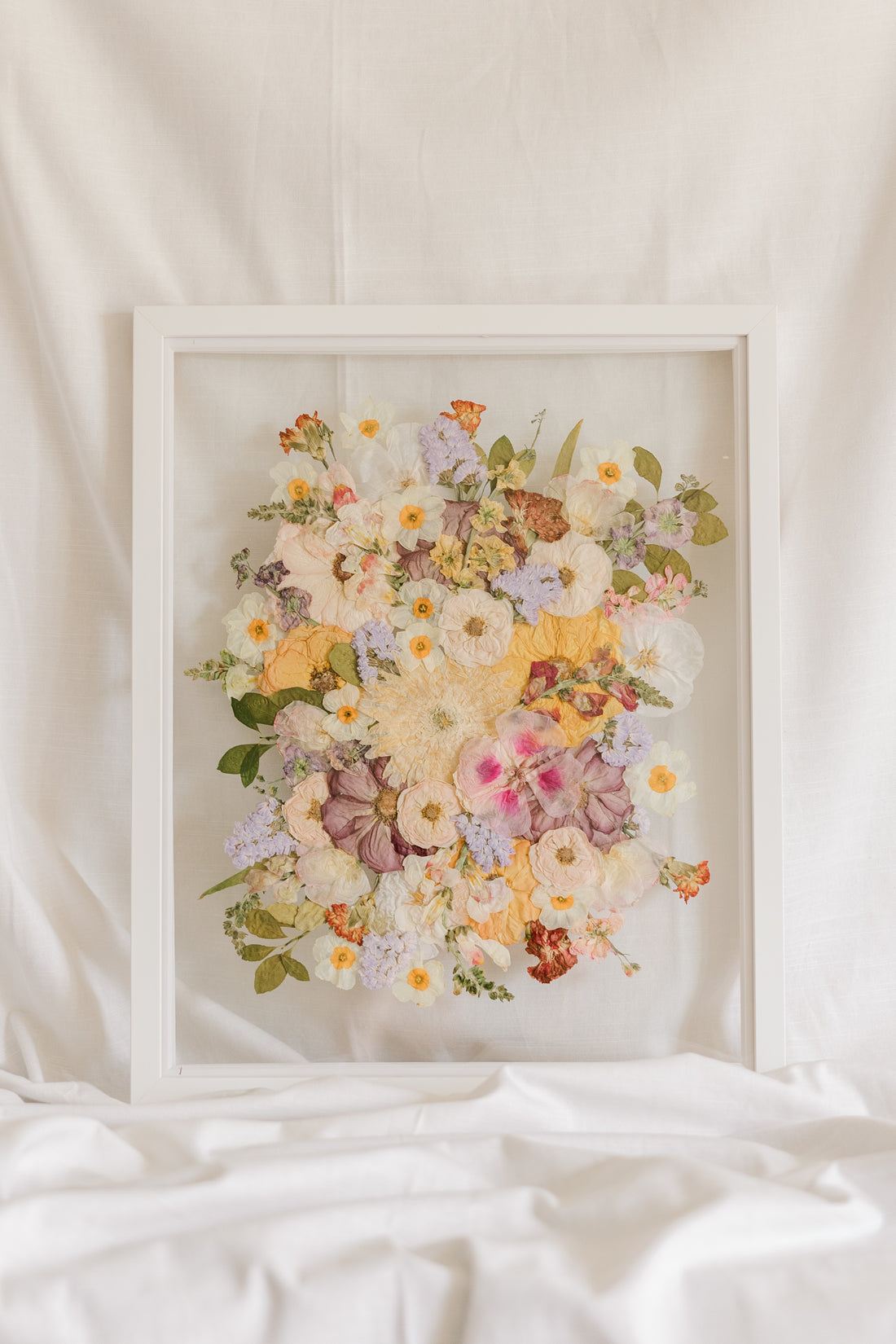 A colorful spring-time pressed bouquet on display in a white wood glass floating frame.