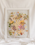 A colorful spring-time pressed bouquet on display in a white wood glass floating frame.