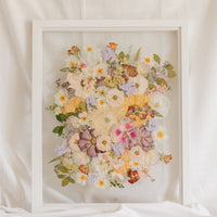 A colorful spring-time pressed bouquet on display in a white wood glass floating frame.