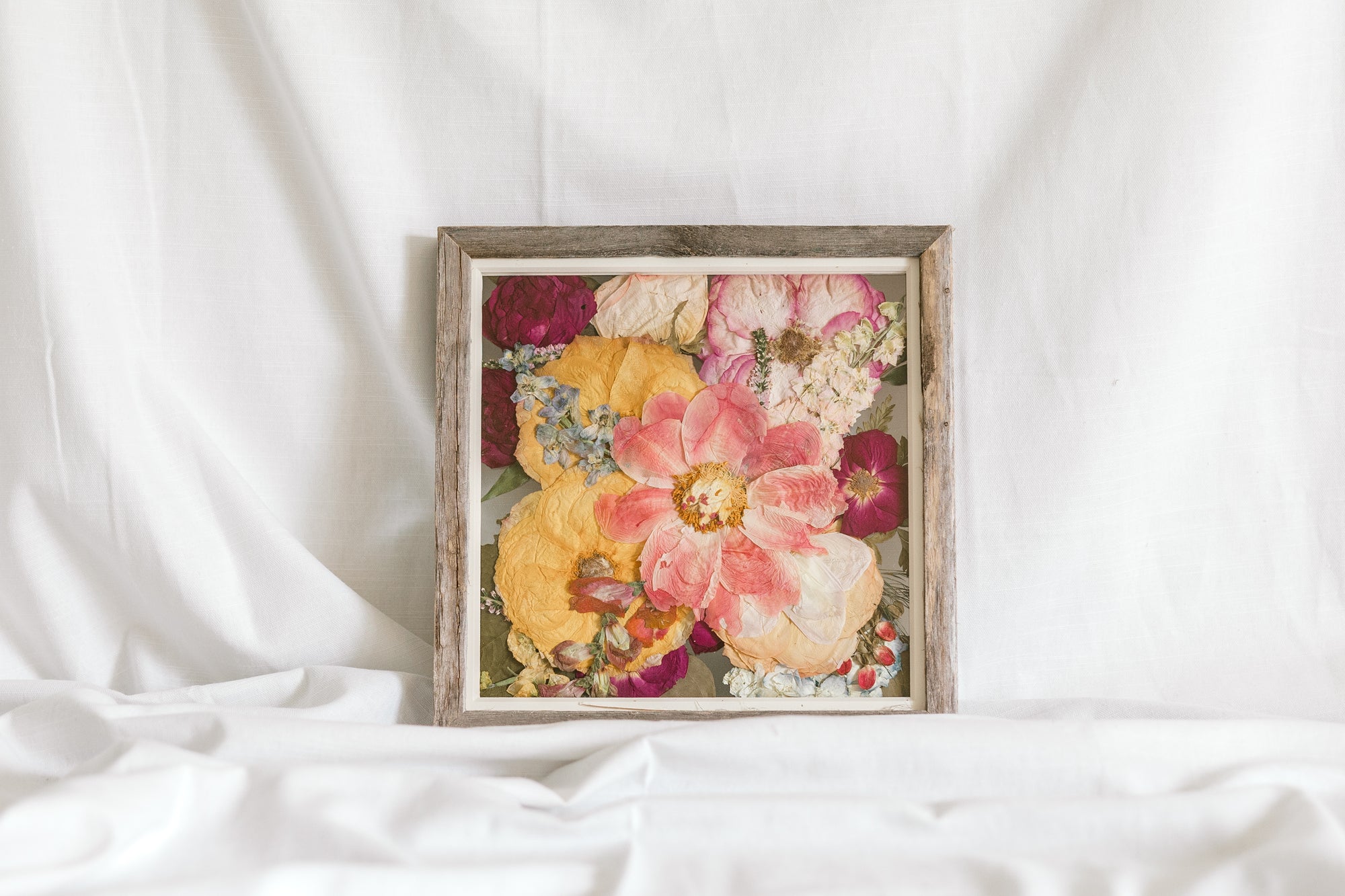 A colorful pressed flower arrangement in a barnwood frame made by the Pressed Bouquet Shop. 