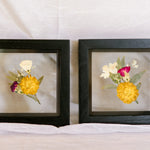 Two boutonnieres pressed and preserved in 6x6" black wood frames.