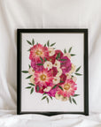 A bright pink and white bouquet is detailed by sprouts of greenery as they have been pressed and framed inside this bouquet preservation black wood frame with an archival grade background.