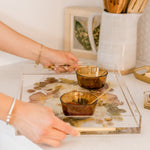 Hands carrying a preserved flower resin serving tray with two small dishes on it. 