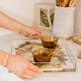 Hands carrying a preserved flower resin serving tray with two small dishes on it. 