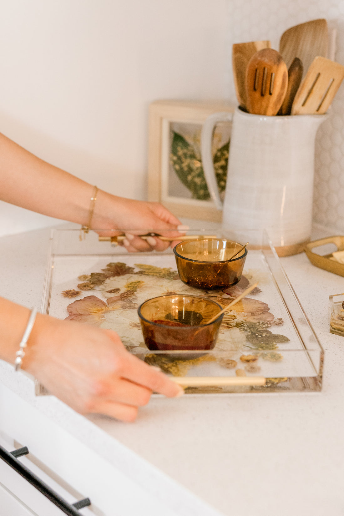 Hands carrying a preserved flower resin serving tray with two small dishes on it. 