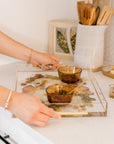 Hands carrying a preserved flower resin serving tray with two small dishes on it. 