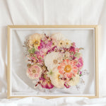 A bright pink and white pressed flower arrangement from a wedding bouquet is centered inside this gold wood frame.