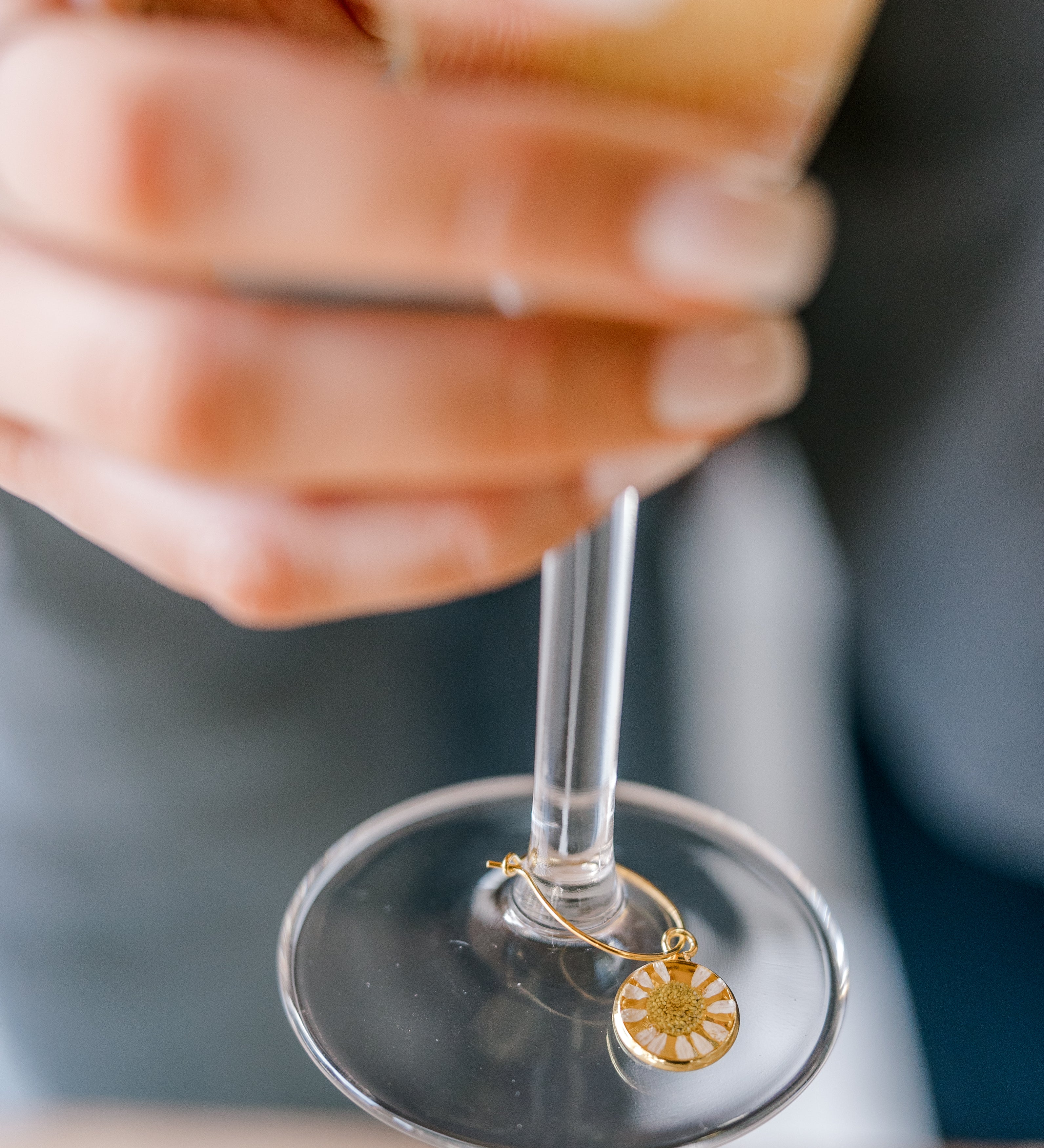 A woman is holding a glass of champagne with a pressed flower drink charm. The charm features a real small white flower. 