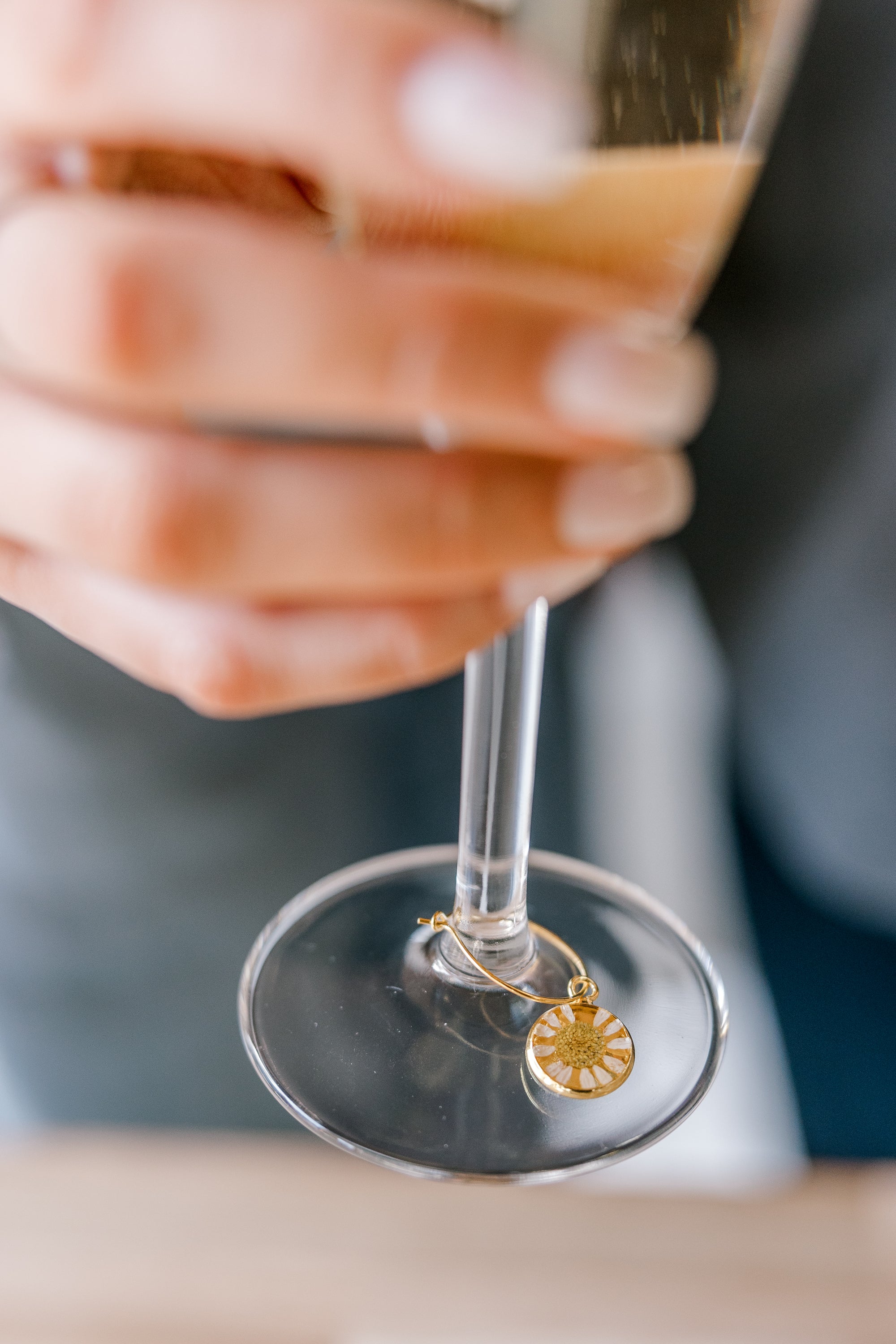 A woman is holding a glass of champagne with a pressed flower drink charm. The charm features a real small white flower. 