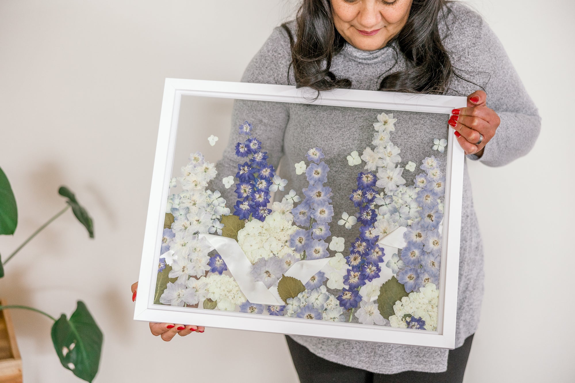 A field style pressed flower frame with pressed hydrangea and pressed delphinium detailed by a ribbon intertwined through the pressed flowers. 