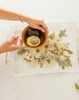 Wedding bouquet preserved in resin as a serving tray with gold handles. In the photo hands are maneuvering a brown bowl with a avocado cut in half.