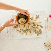 Wedding bouquet preserved in resin as a serving tray with gold handles. In the photo hands are maneuvering a brown bowl with a avocado cut in half.