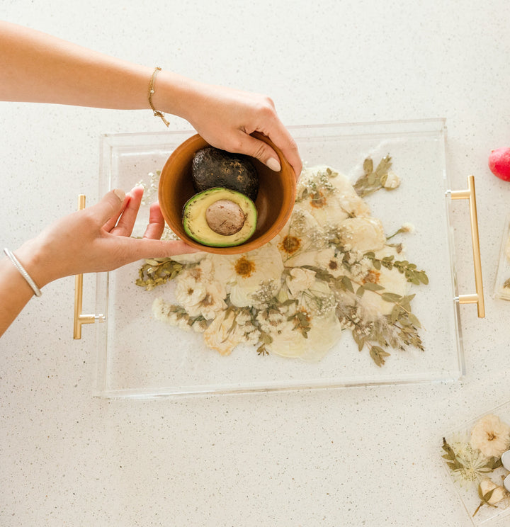 Wedding bouquet preserved in resin as a serving tray with gold handles. In the photo hands are maneuvering a brown bowl with a avocado cut in half.