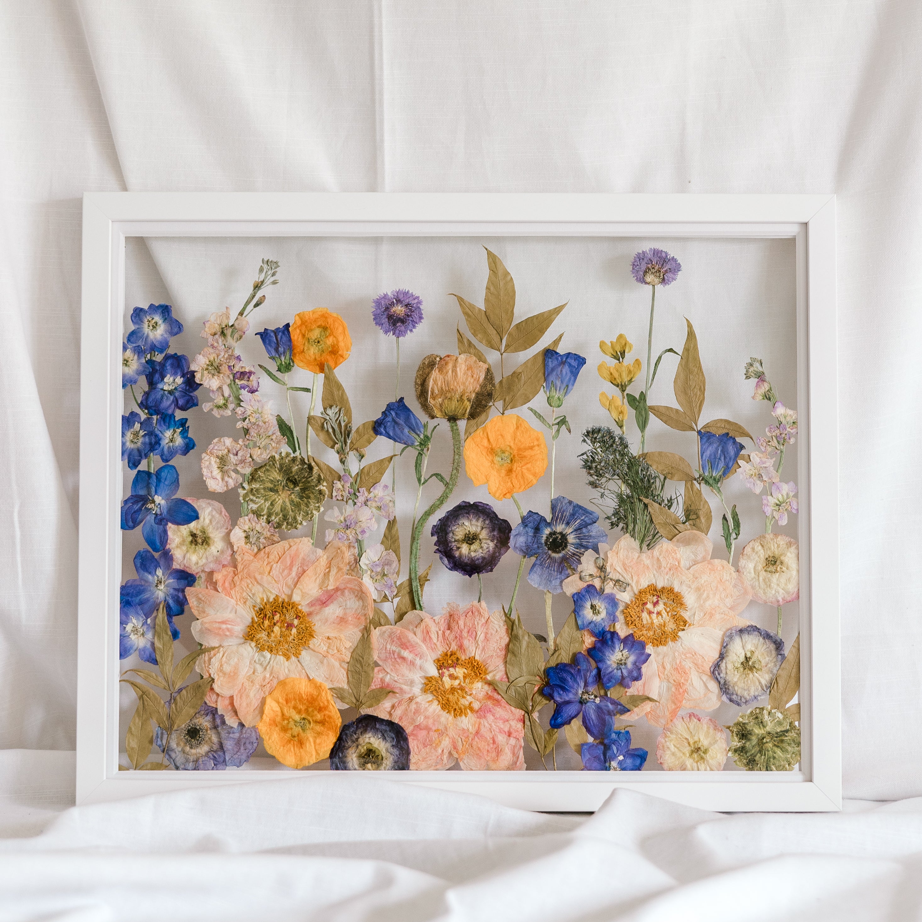 A colorful wedding bouquet turned into a colorful pressed flower display inside a white wood frame.