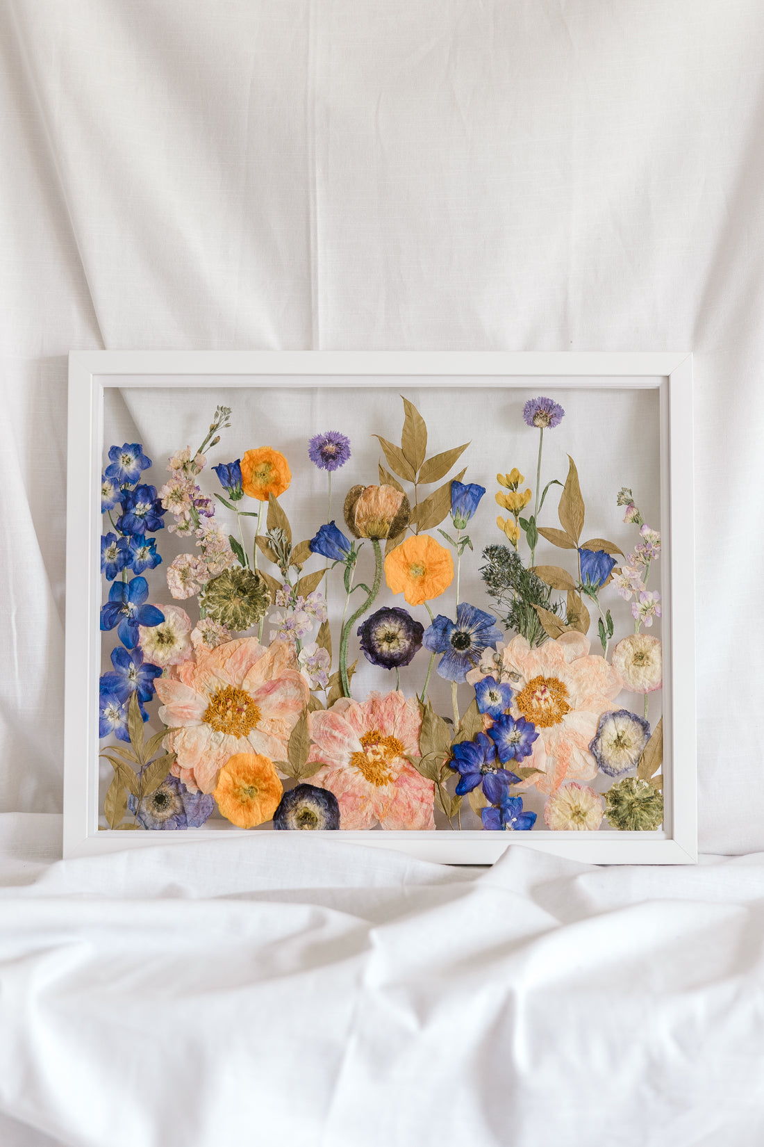 A colorful wedding bouquet turned into a colorful pressed flower display inside a white wood frame.