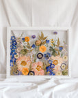 A colorful wedding bouquet turned into a colorful pressed flower display inside a white wood frame.