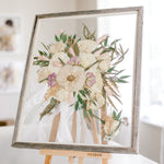 A white and pink wedding bouquet that has been pressed with a boutonniere inside a barn wood frame.