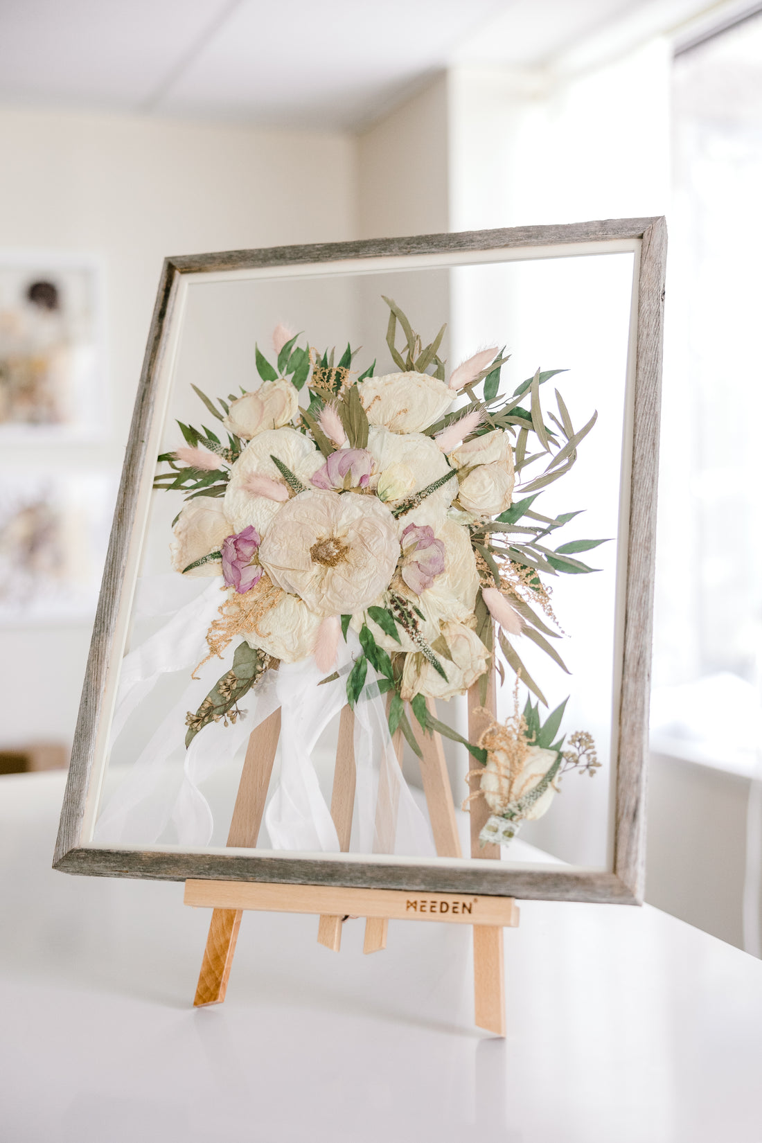 A white and pink wedding bouquet that has been pressed with a boutonniere inside a barn wood frame.