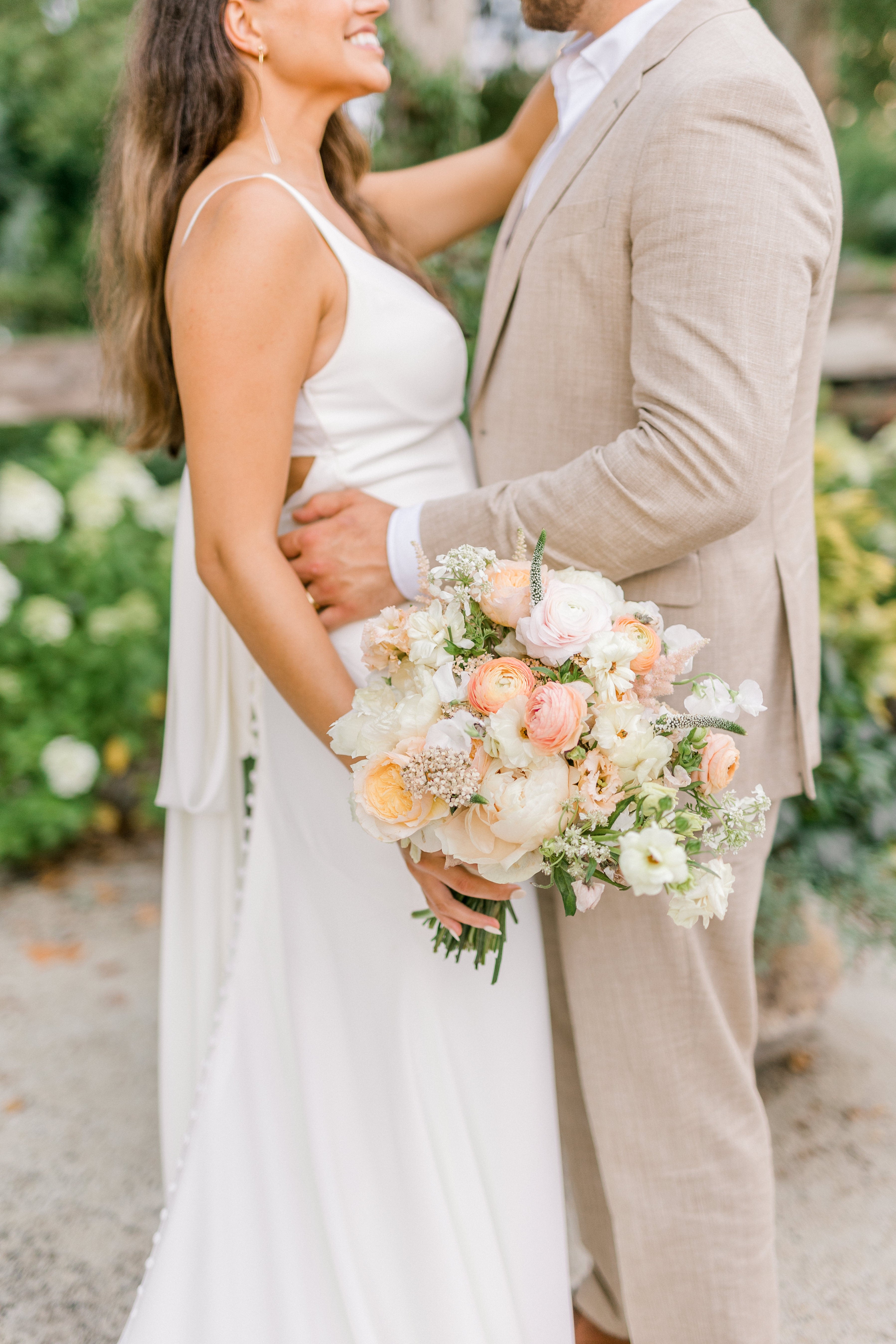 A bride and groom smiling at each other while the bride holds her wedding bouquet. 