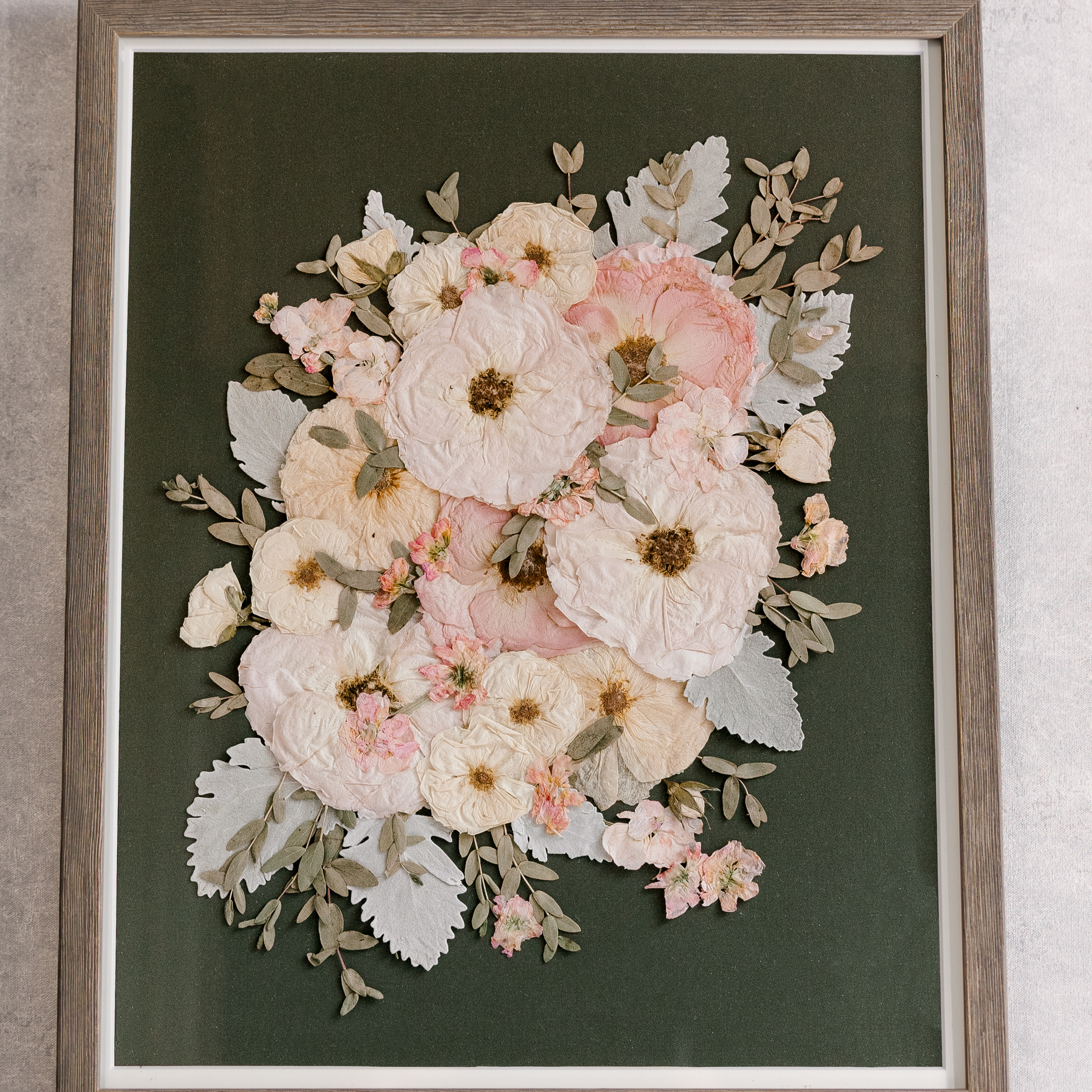 Large wood frame with a green background and pastel pressed flowers inside.