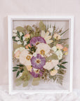 A pink and purple pressed flower frame filled with small detail pressed flowers and plenty of pressed greenery.