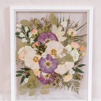 A pink and purple pressed flower frame filled with small detail pressed flowers and plenty of pressed greenery.