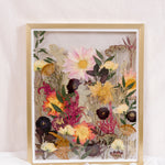 Pressed flowers are displayed as if they were growing from the ground in this gold wood floating frame.