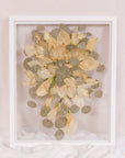 A frame filled with pressed calla lillies displayed in a white wood surround.