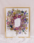 Purple and blue flowers have been pressed and surround an invitation in this bouquet preservation piece. 