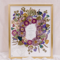 Purple and blue flowers have been pressed and surround an invitation in this bouquet preservation piece. 