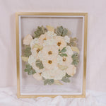 An all white bouquet of flowers has been pressed into a preserved piece of art. 