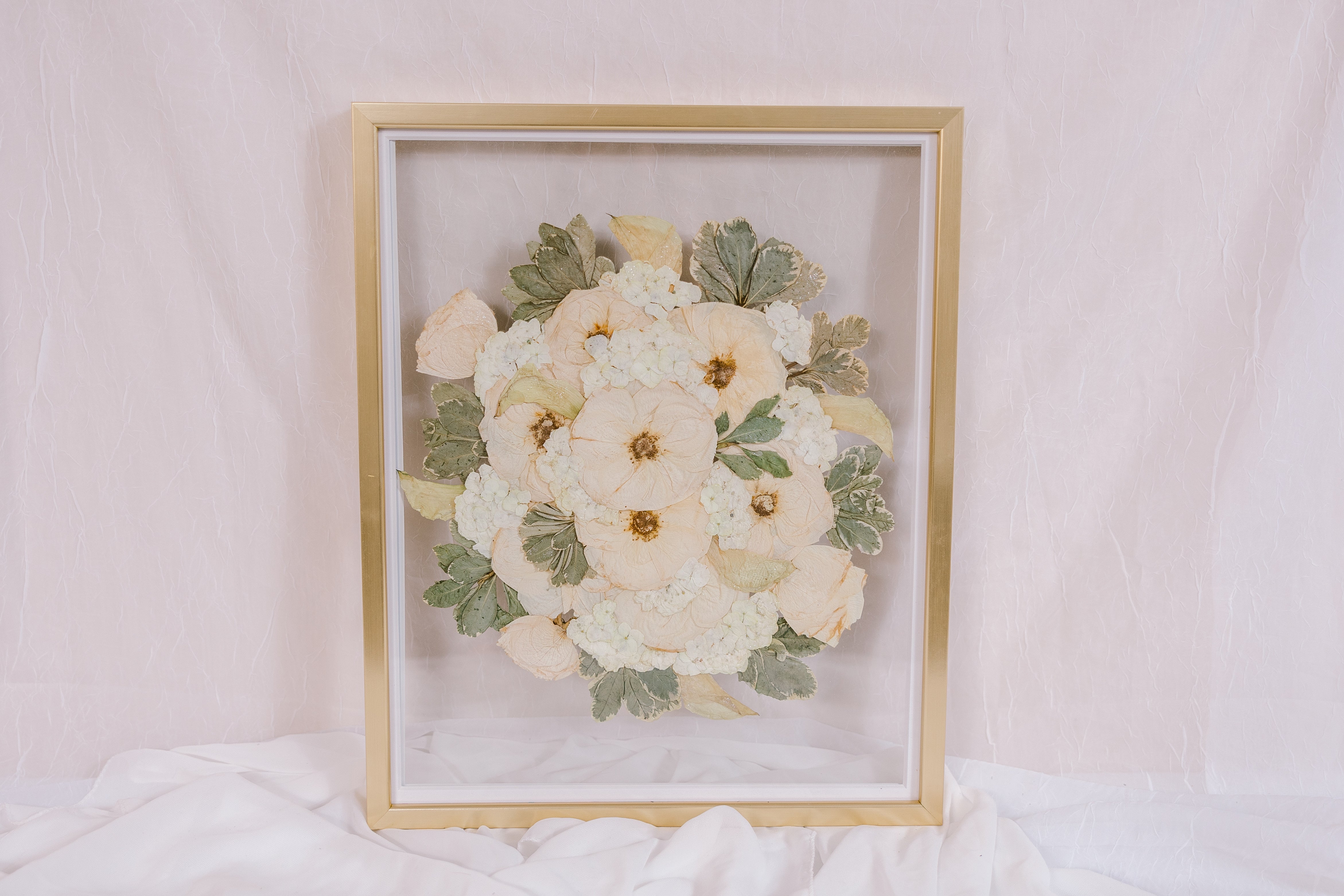 An all white bouquet of flowers has been pressed into a preserved piece of art. 