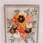 A vibrant pressed flower arrangement inside a barn wood frame. 