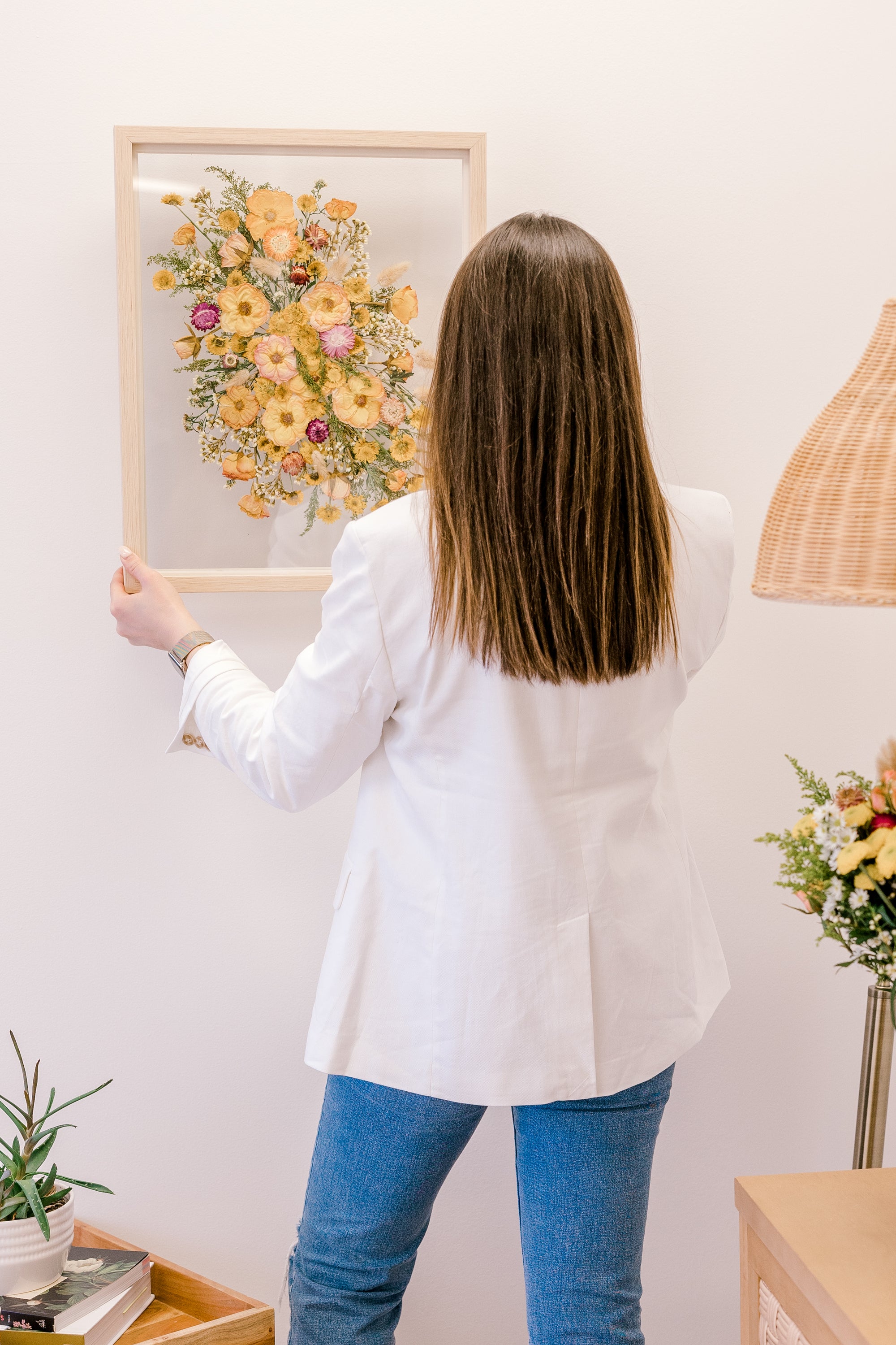 A woman holding a bright flower bouquet that has been pressed and put inside a frame. 