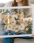 A close up of a pressed flower frame being held by a woman sitting on a sofa.