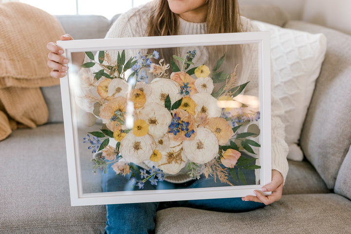 A close up of a pressed flower frame being held by a woman sitting on a sofa.