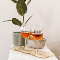 Two glasses of wine sitting on a resin display tray on an end table with a plant in the background. 