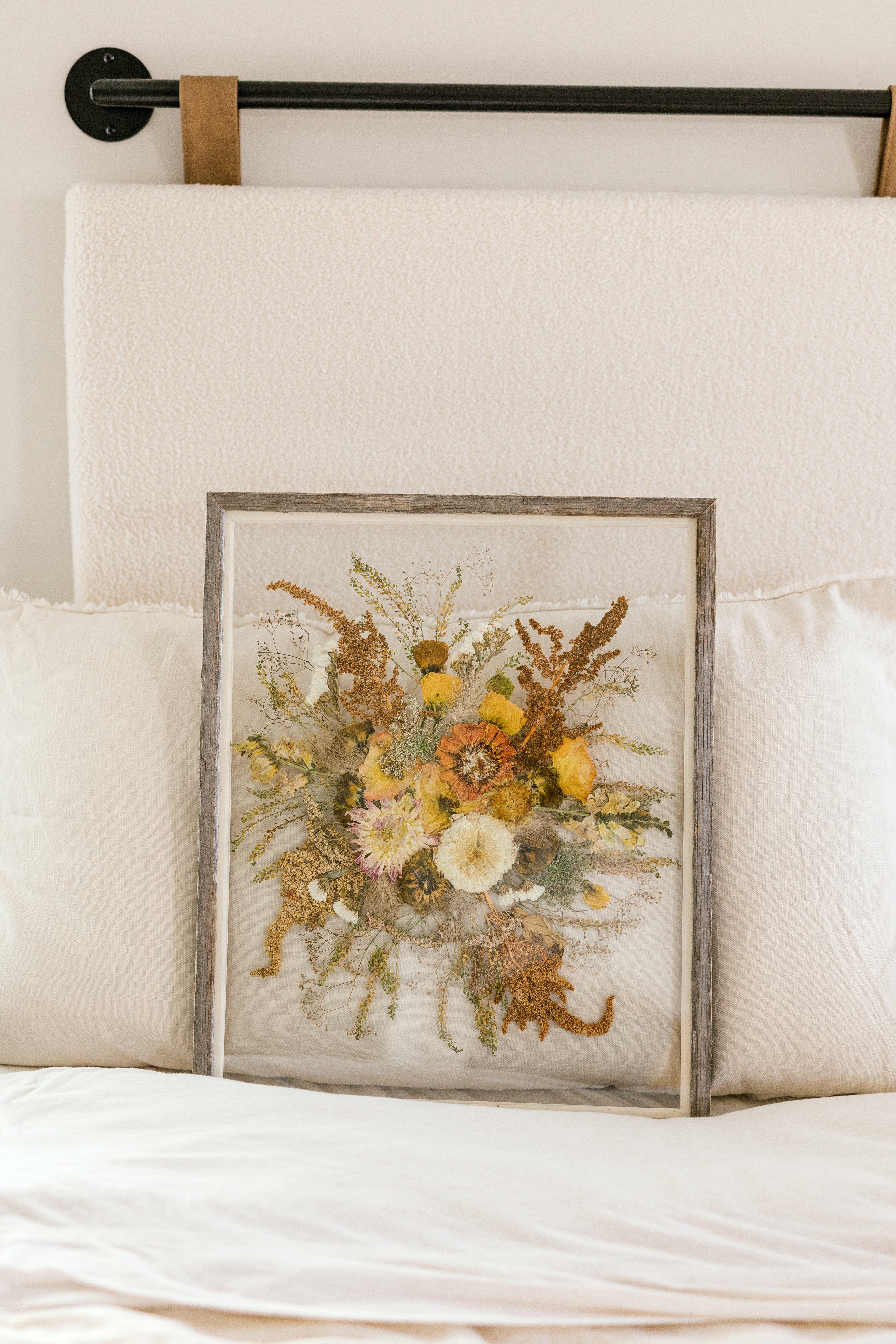 A fall pressed bouquet sitting against pillows on a bed.  