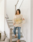 Woman standing on staircase holding a pressed wedding bouquet in a frame. 