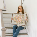 A woman sitting on a staircase admiring her pressed wedding flowers in a barn wood frame with a date addition in the bottom right corner. 