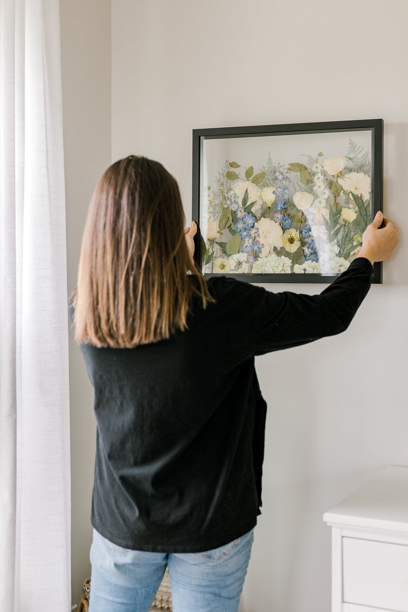 A woman hangs a preserved bouquet arrangement on her wall. 