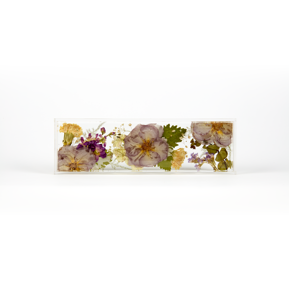 A delicate design of pressed purple, white, and green florals in a resin display tray as a part of a wedding bouquet preservation order. 
