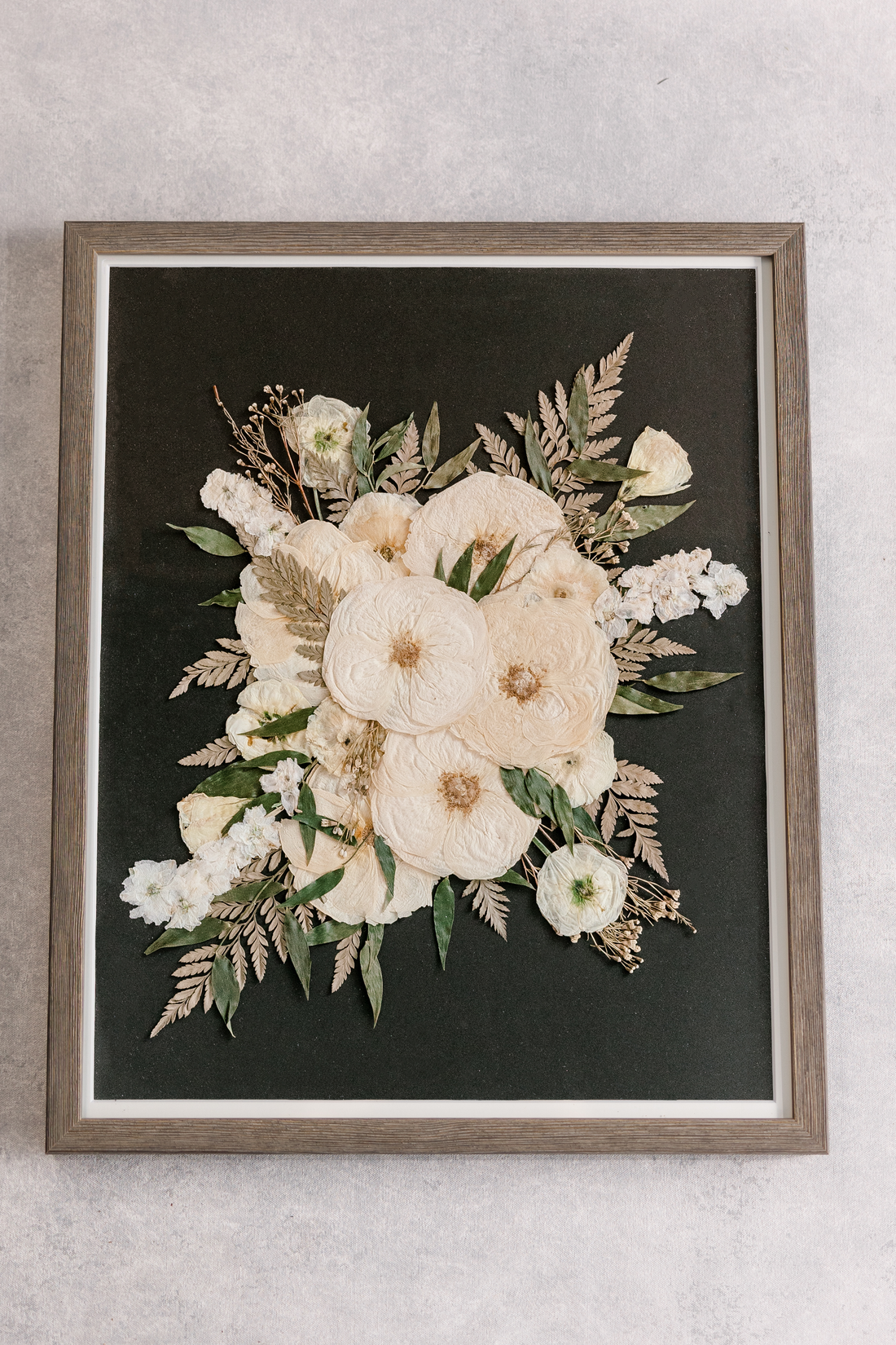 A large wood frame with pressed white and green florals against a black background.