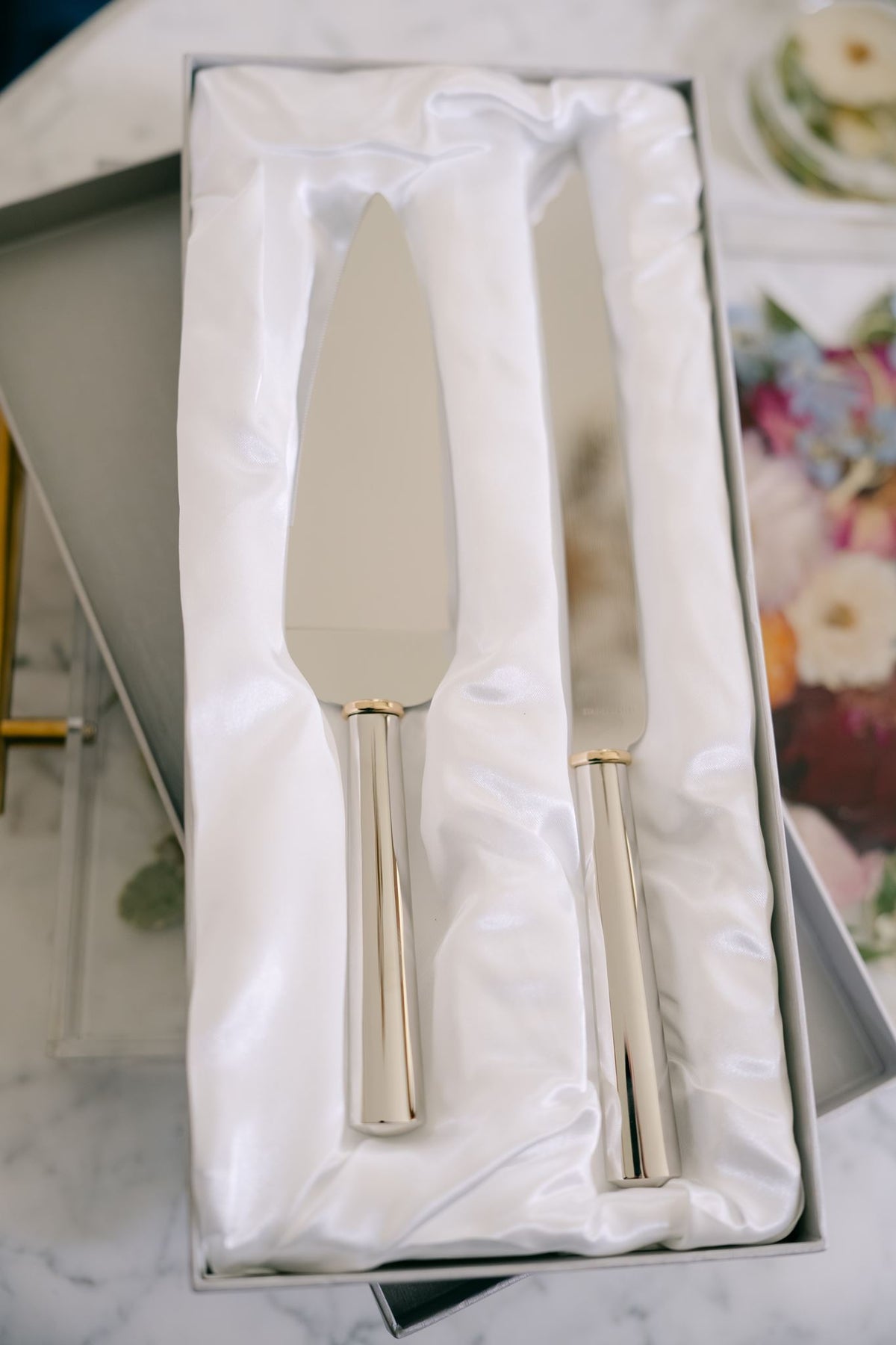 Gold ring handled wedding cake knife and server set from Element Marketplace, shown in gift box, in front of resin serving tray
