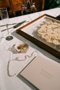 Hardcover wedding guest book in beige from Element Marketplace, shown on a table with pressed floral products, frame and coaster, and a champagne flute
